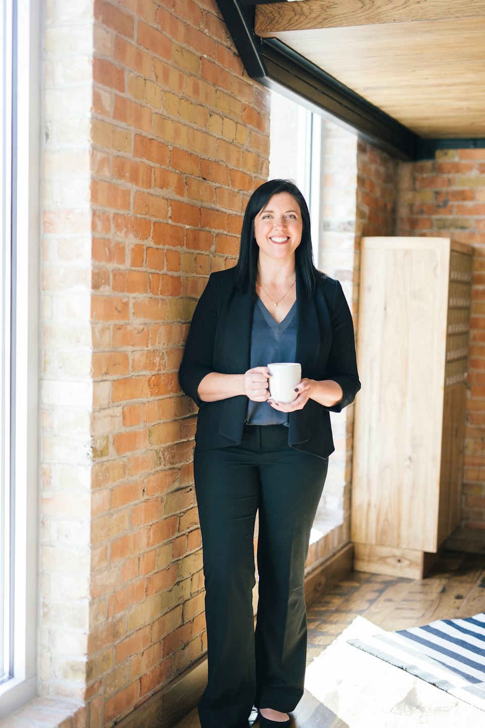Woman in business attire holding a mug in a modern office.