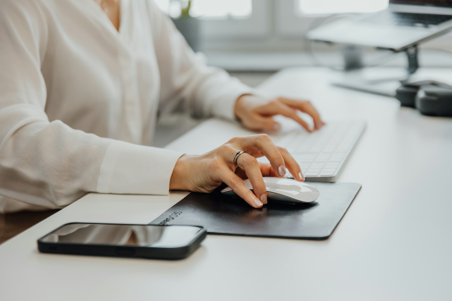 Woman typing on a keyboard with a mouse and smartphone on a desk.